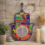 Hamsa multicolor 43764 con edificios de Jerusalem y Bircat Habait en hebreo, ambientada sobre un muro de piedra.